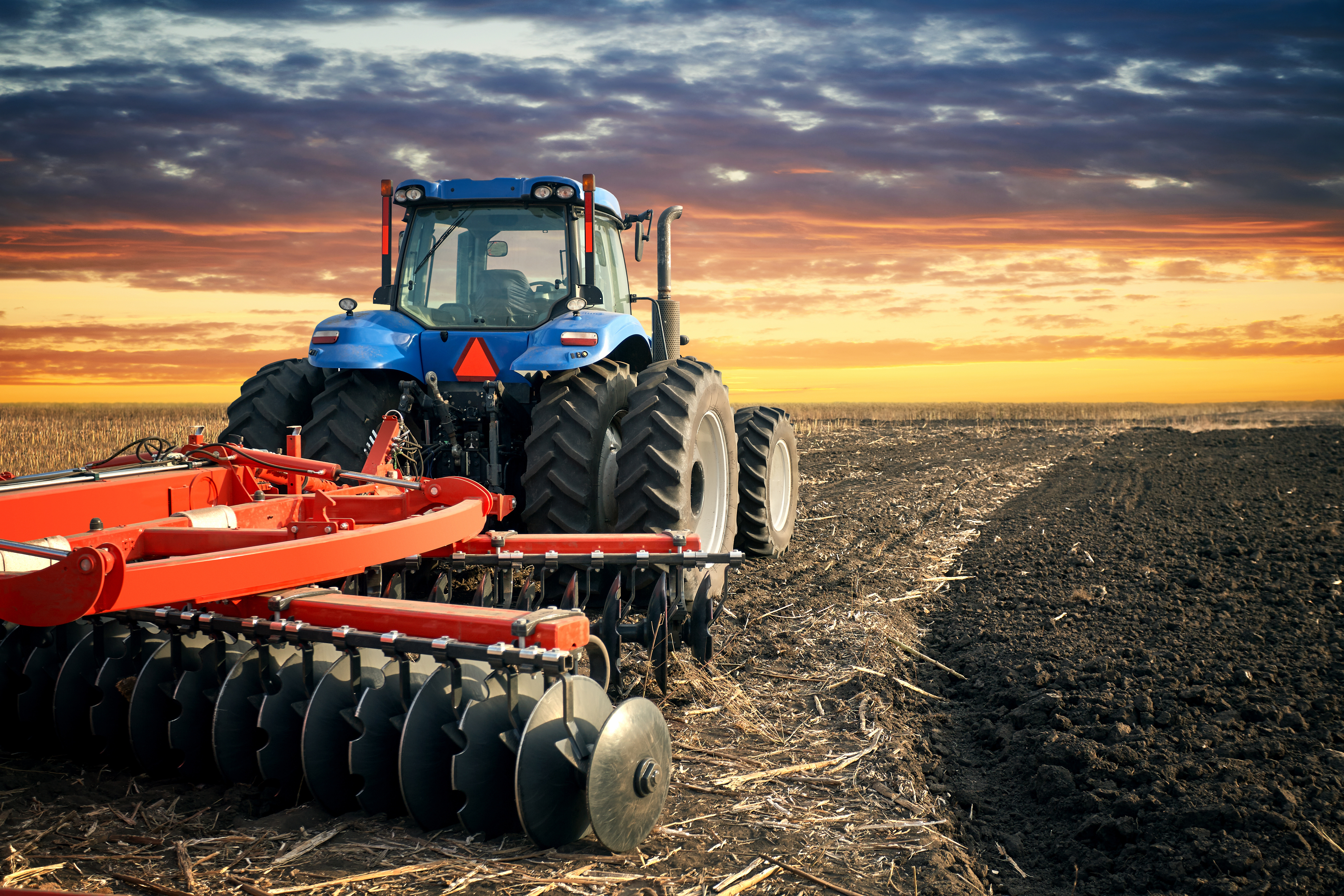 Tractor plowing field on sunset background